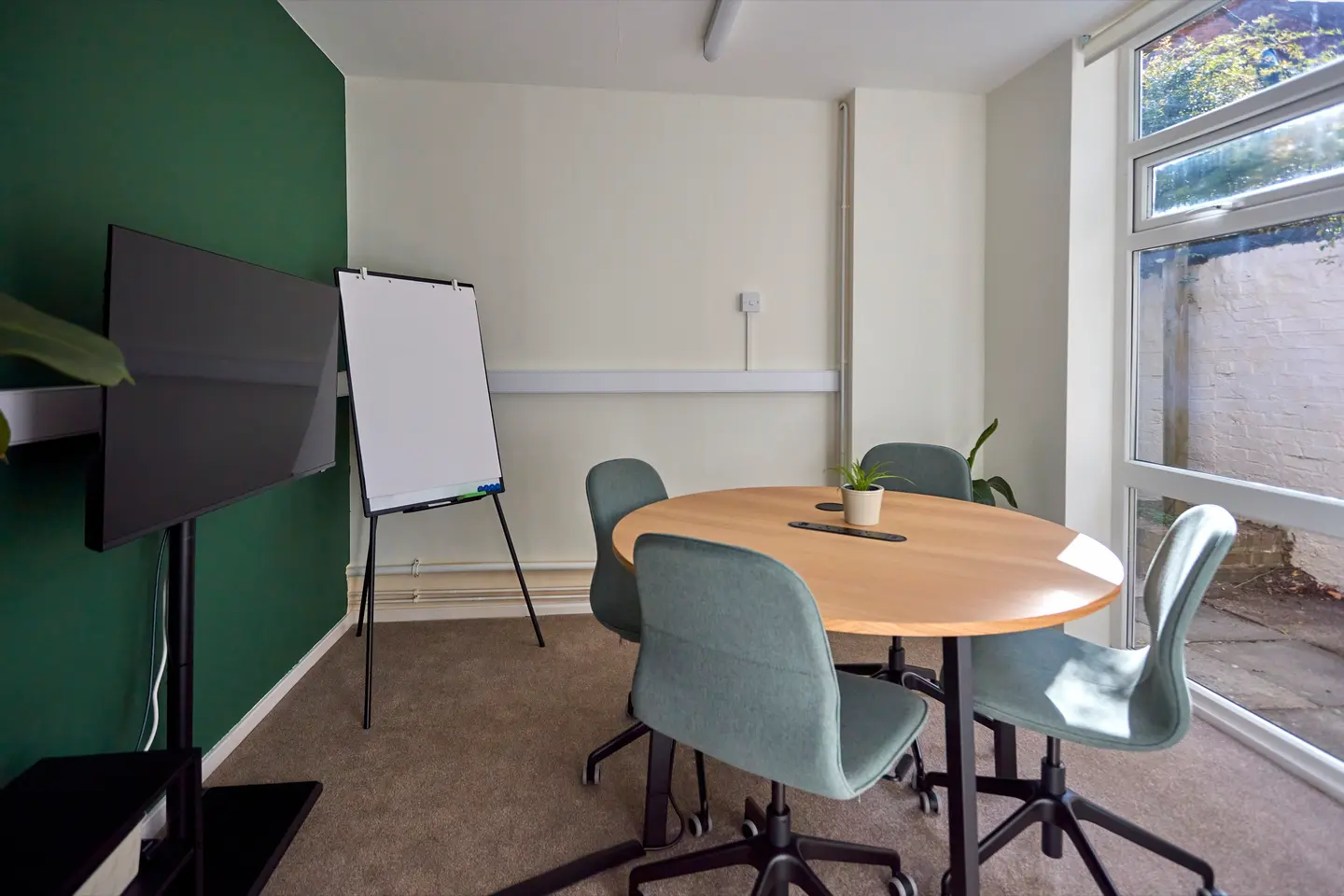 The meeting room at Pershore Coworking, with a round table, screen, flipchart, and a window onto the garden
